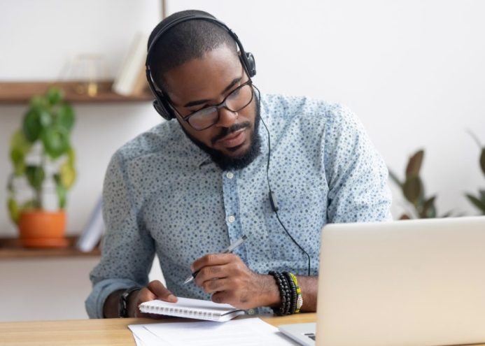 Focused african businessman in headphones writing notes watching webinar Carer on a laptop
